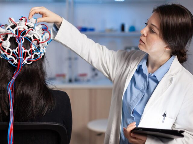 back-view-woman-patient-wearing-performant-eeg-headset-sitting-chair-neurological-research-laboratory-while-medical-researcher-adjusting-it-examining-nervous-system-typing-tablet_482257-16437